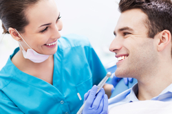 A male patient smiling while being treated by a female dentist, who appears to be administering a dental exam